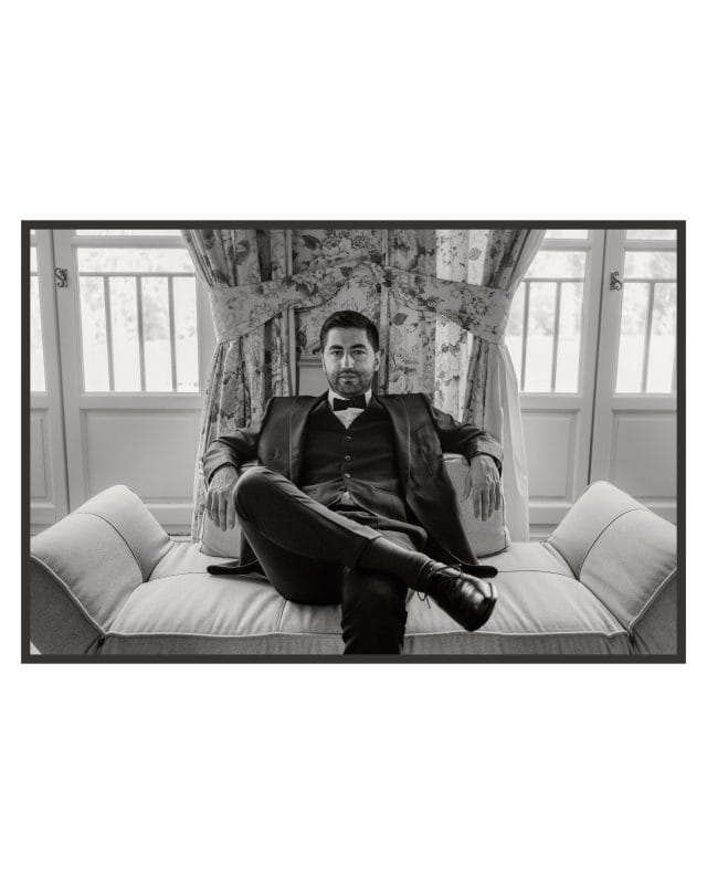 Portrait en noir et blanc de Geoffrey assis les jambes croisées sur une banquette, devant les fenêtres du château de la Berchère.