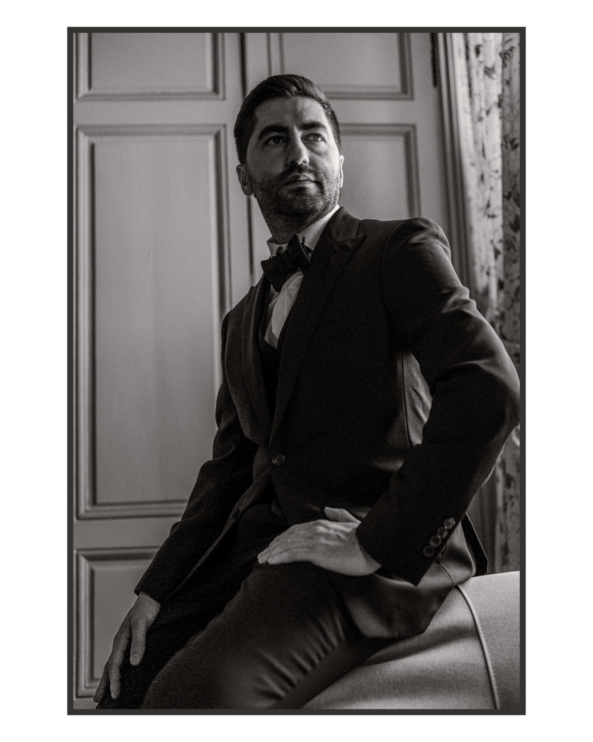 Geoffrey assis en costume, le regard tourné sur le côté, dans un portrait vertical en noir et blanc réalisé pendant son mariage à Nuits-Saint-Georges.